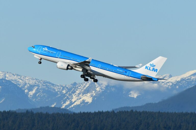 A blue and white airplane flying over a mountain range