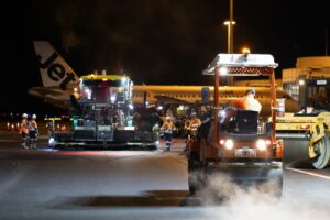 Airport runway resurfacing at night with heavy machinery