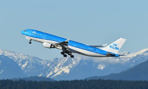 A blue and white airplane flying over a mountain range